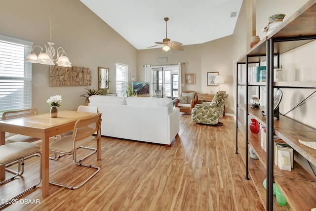 living room with light wood-type flooring, ceiling fan with notable chandelier, and high vaulted ceiling