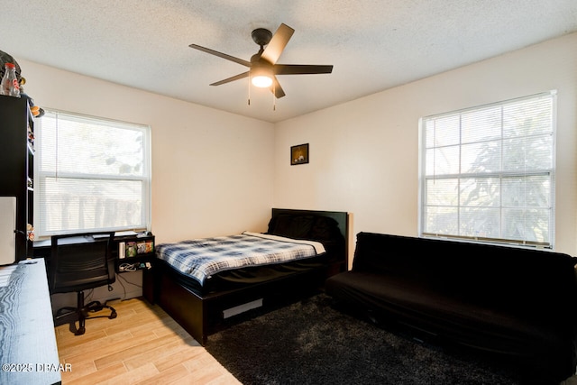 bedroom with multiple windows, a textured ceiling, ceiling fan, and light wood-type flooring