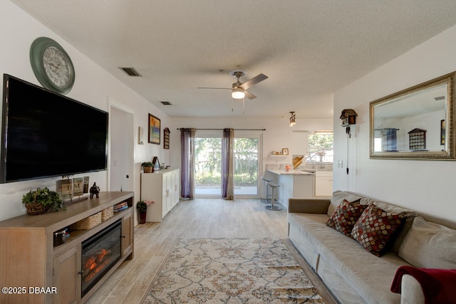 living room with a textured ceiling, ceiling fan, and light hardwood / wood-style flooring