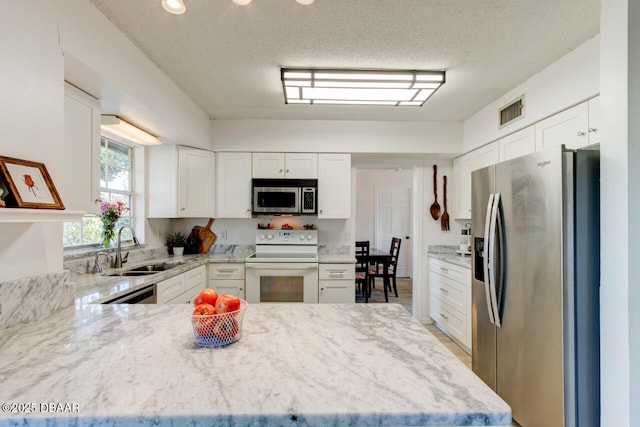 kitchen with stainless steel appliances, a textured ceiling, light stone counters, sink, and white cabinetry