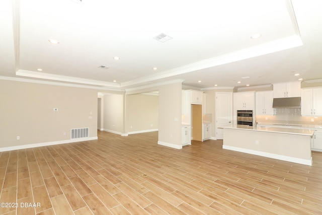 unfurnished living room featuring light wood-type flooring, a raised ceiling, and crown molding