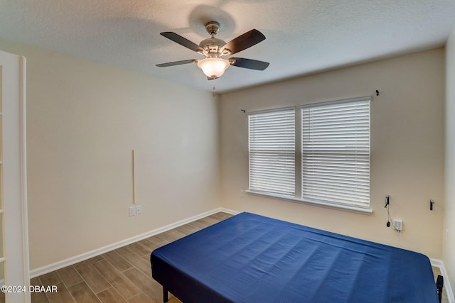 bedroom with baseboards, wood finished floors, a textured ceiling, and ceiling fan
