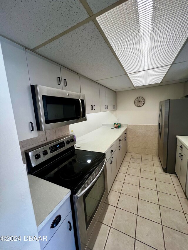 kitchen featuring a drop ceiling, stainless steel appliances, tile walls, light tile patterned floors, and white cabinetry