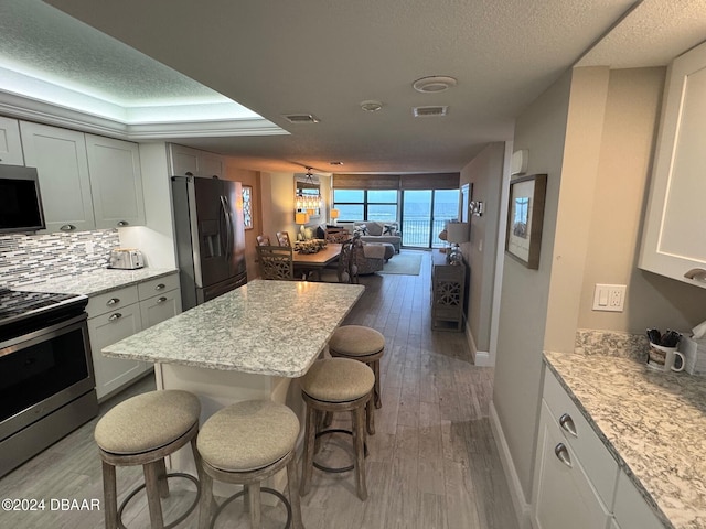 kitchen with decorative backsplash, appliances with stainless steel finishes, a kitchen breakfast bar, light stone counters, and hardwood / wood-style flooring