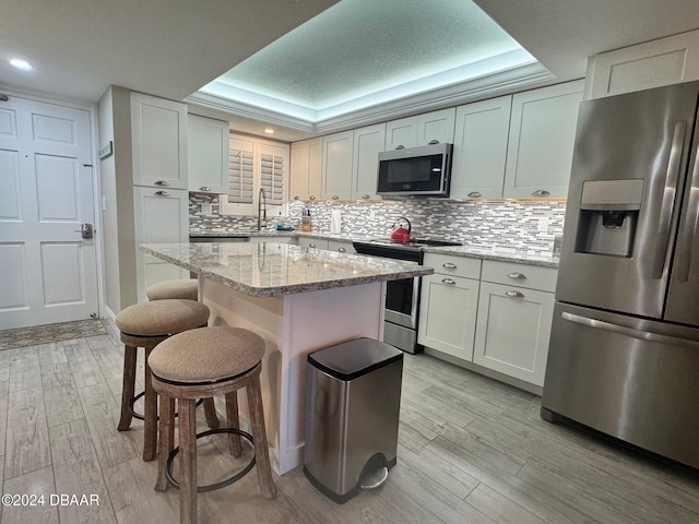 kitchen featuring white cabinetry, a raised ceiling, light stone countertops, and appliances with stainless steel finishes