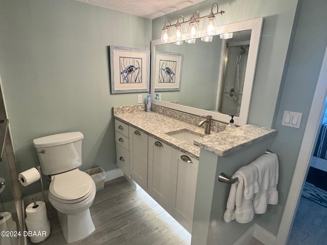 bathroom featuring walk in shower, wood-type flooring, a textured ceiling, toilet, and vanity