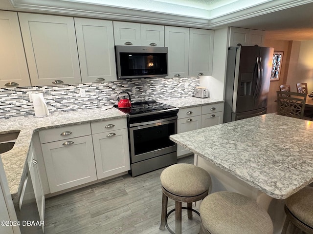 kitchen featuring a kitchen bar, stainless steel appliances, light stone counters, and tasteful backsplash