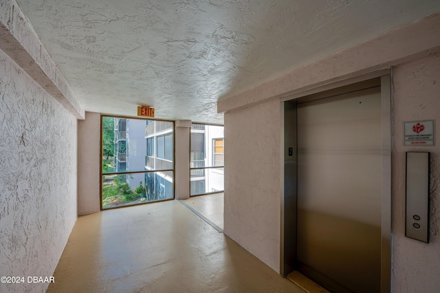 hallway featuring a textured ceiling, elevator, a wall of windows, concrete flooring, and a textured wall