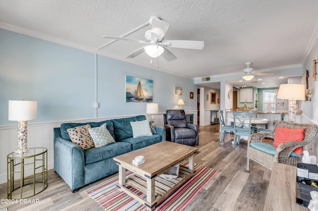 living room featuring ceiling fan, crown molding, a textured ceiling, and light wood-type flooring