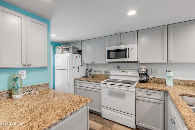 kitchen with light stone countertops, white appliances, and light hardwood / wood-style flooring