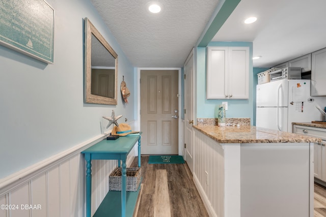 kitchen featuring white cabinets, wood-type flooring, white refrigerator, and light stone counters