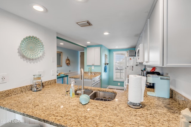 kitchen with kitchen peninsula, light stone counters, sink, and white cabinets