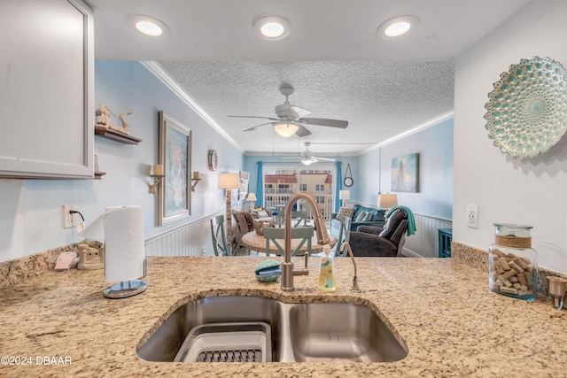 kitchen featuring light stone countertops, ornamental molding, a textured ceiling, ceiling fan, and sink