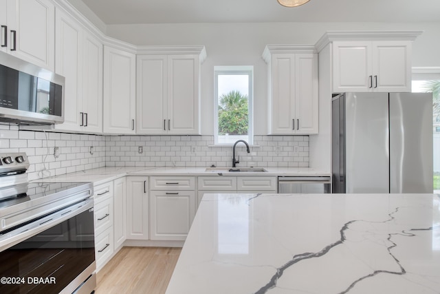 kitchen featuring white cabinets, appliances with stainless steel finishes, light stone counters, and sink