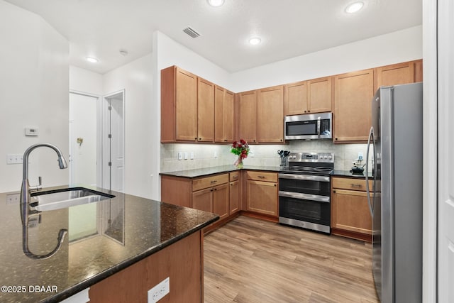 kitchen featuring a sink, light wood-type flooring, appliances with stainless steel finishes, and decorative backsplash