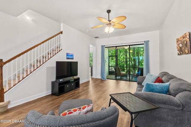 living area with wood finished floors, visible vents, baseboards, a ceiling fan, and stairs