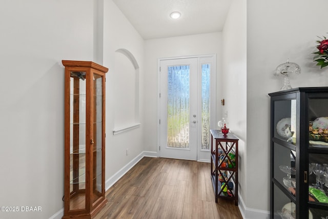 foyer with baseboards, arched walkways, and wood finished floors