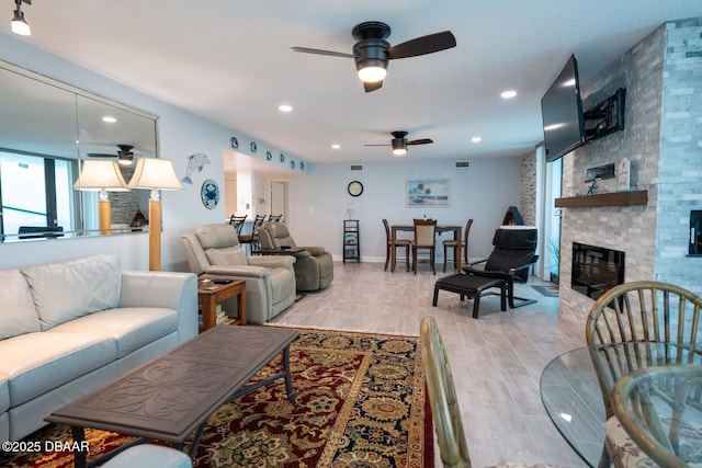 living room featuring ceiling fan, a stone fireplace, and light hardwood / wood-style flooring