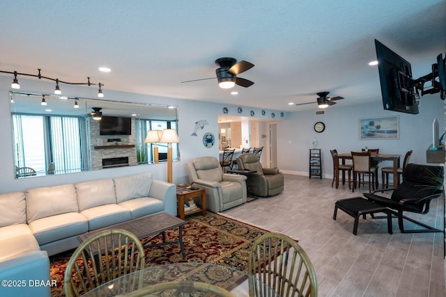 living room with ceiling fan, a fireplace, light hardwood / wood-style flooring, and rail lighting