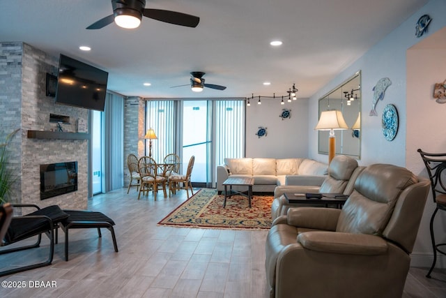 living room featuring wood-type flooring, ceiling fan, a fireplace, and a wall of windows