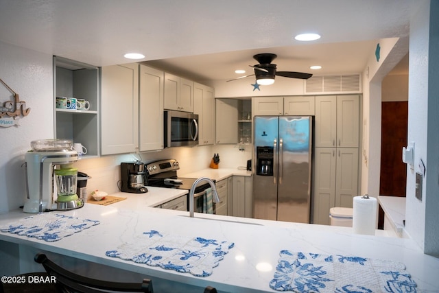 kitchen featuring gray cabinets, decorative backsplash, ceiling fan, kitchen peninsula, and stainless steel appliances