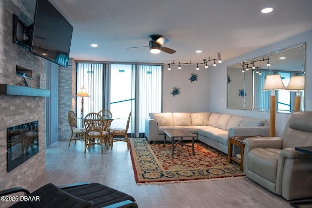 living room with a wall of windows, a large fireplace, track lighting, ceiling fan, and hardwood / wood-style floors