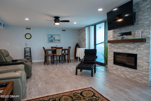 living room featuring a stone fireplace, ceiling fan, and a wall of windows