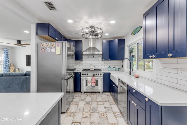 kitchen featuring blue cabinetry, appliances with stainless steel finishes, sink, and wall chimney range hood