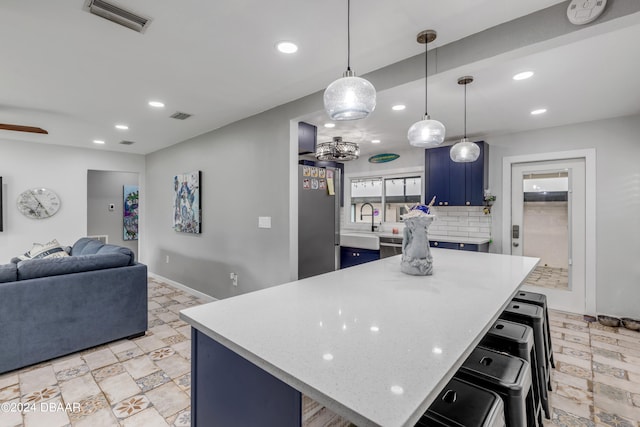 kitchen featuring stainless steel refrigerator, a breakfast bar area, backsplash, a kitchen island, and blue cabinets