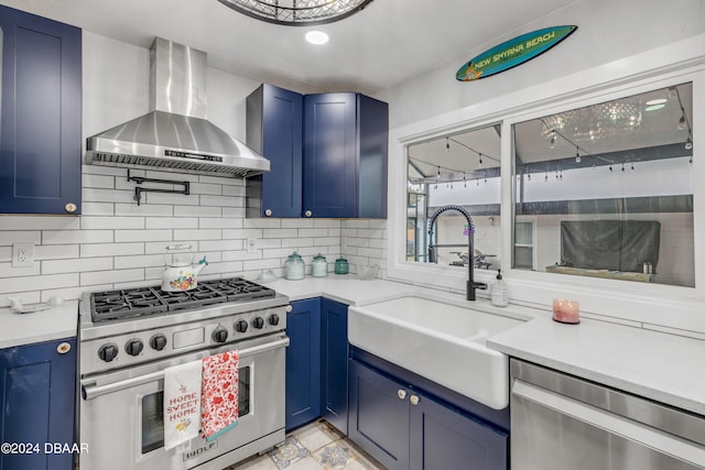 kitchen with stainless steel appliances, sink, backsplash, blue cabinets, and wall chimney range hood