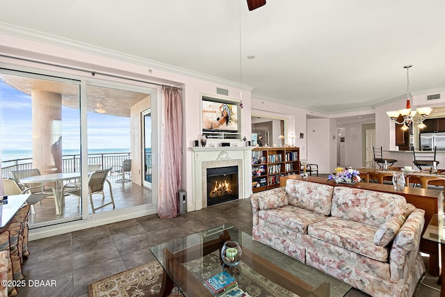 living room with a water view, crown molding, a tiled fireplace, and an inviting chandelier