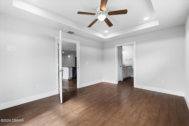 unfurnished bedroom with ensuite bathroom, dark hardwood / wood-style flooring, a raised ceiling, and ceiling fan