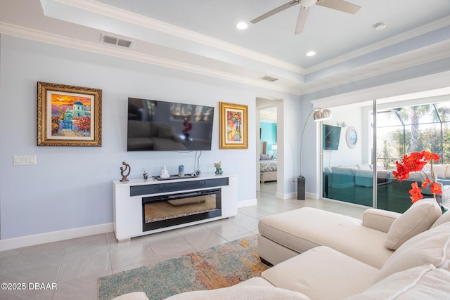 tiled living room with ceiling fan, ornamental molding, and a tray ceiling