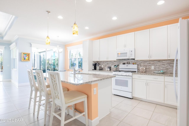 kitchen featuring white appliances, decorative light fixtures, white cabinets, and a center island with sink