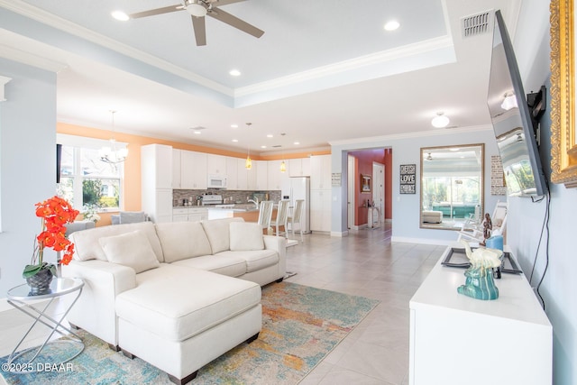 tiled living room with a raised ceiling, ornamental molding, and ceiling fan with notable chandelier