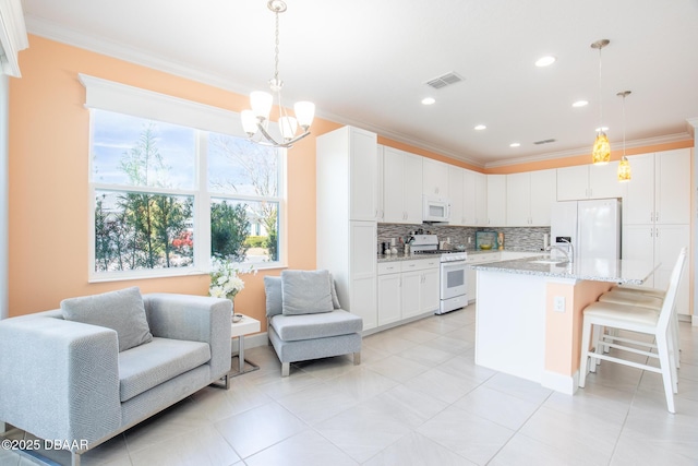 kitchen with pendant lighting, white appliances, light stone counters, an island with sink, and white cabinets