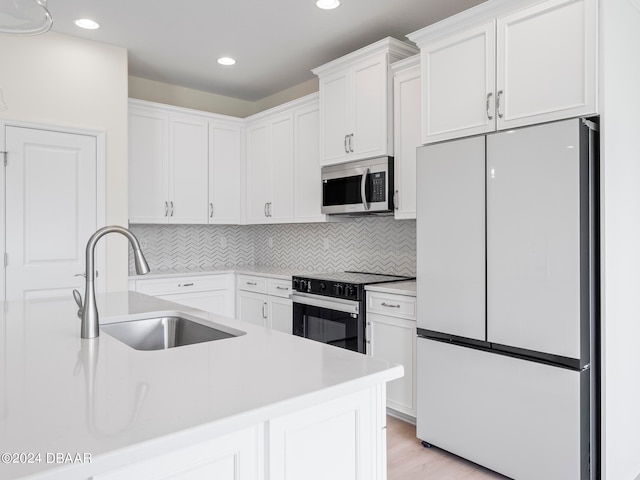 kitchen featuring white cabinetry, sink, appliances with stainless steel finishes, light wood-type flooring, and decorative backsplash