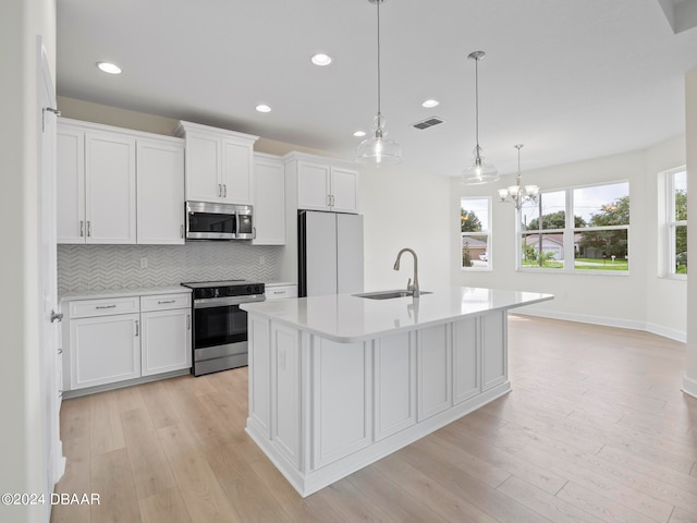 kitchen with pendant lighting, sink, an island with sink, white cabinetry, and appliances with stainless steel finishes