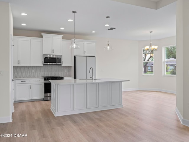 kitchen featuring stainless steel appliances, white cabinetry, a center island with sink, and decorative light fixtures