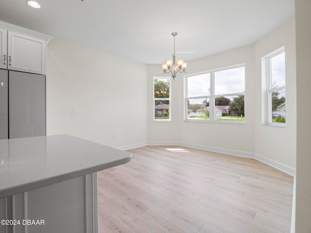 unfurnished dining area featuring light wood-type flooring and a notable chandelier