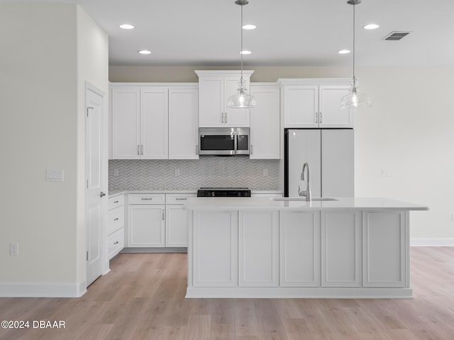 kitchen with white fridge, hanging light fixtures, sink, white cabinets, and a kitchen island with sink