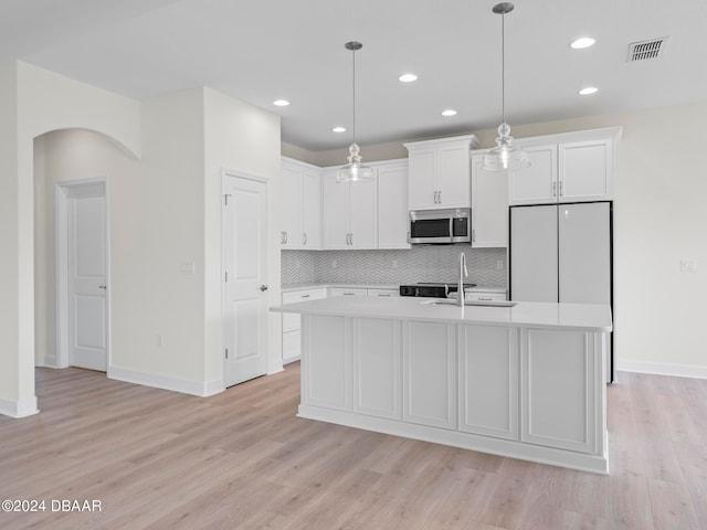 kitchen featuring light wood-type flooring, hanging light fixtures, a center island with sink, and white cabinets