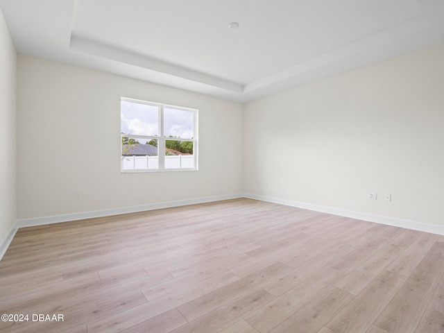 empty room with light hardwood / wood-style flooring and a tray ceiling