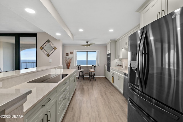 kitchen with white cabinets, light wood-style floors, light stone counters, black appliances, and recessed lighting