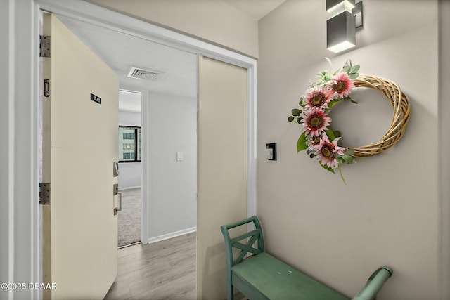 hall with wood finished floors, visible vents, and baseboards