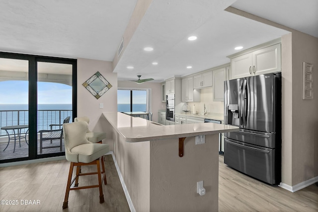 kitchen featuring stainless steel appliances, a breakfast bar, light wood-style flooring, and white cabinets