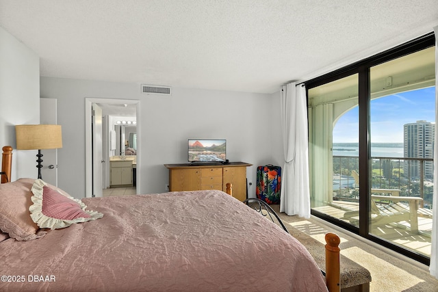 bedroom with a textured ceiling, ensuite bathroom, visible vents, access to outside, and a wall of windows