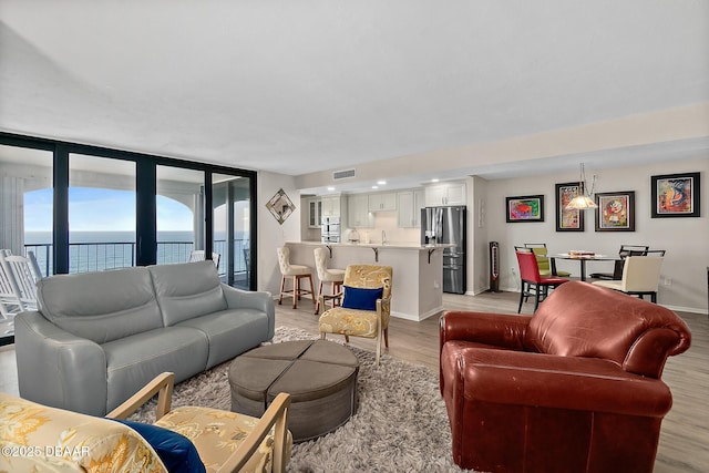 living room with light wood finished floors, a water view, visible vents, and baseboards