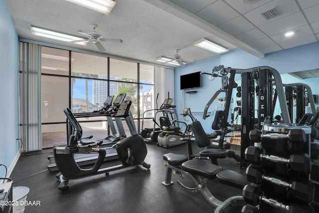 gym featuring a textured ceiling, a drop ceiling, visible vents, a ceiling fan, and expansive windows