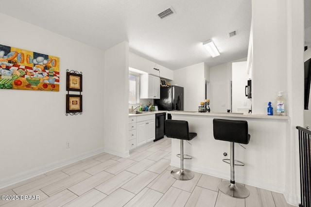 kitchen featuring a breakfast bar, white cabinetry, black appliances, a textured ceiling, and kitchen peninsula